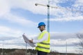 Architect or Engineer man holding blueprints on the Construction Site. Wearing protection clothes. Crane on background over blue Royalty Free Stock Photo