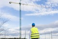 Architect or Engineer man holding blueprints on the Construction Site. Wearing protection clothes. Crane on background over blue Royalty Free Stock Photo