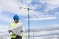 Architect or Engineer man holding blueprints on the Construction Site. Wearing protection clothes. Crane on background over blue Royalty Free Stock Photo