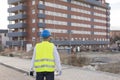 Architect or Engineer man holding blueprints and tablet on the Construction Site. Wearing protection clothes. Crane on background