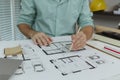 An architect in a green shirt points with a pencil on a house blueprint spread on the table. The image conveys accuracy, Royalty Free Stock Photo