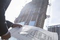 Architect holding blueprint of building at a construction site, midsection