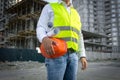 Architect in jacket posing with red helmet at construction site