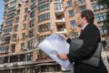 Architect looking at plan and apartment building.