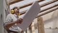 Architect man at work, wearing helmet and headphones looking at blueprint , check the construction house project plan, in Royalty Free Stock Photo