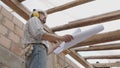 Architect man at work, wearing helmet and headphones looking at blueprint , check the construction house project plan, in Royalty Free Stock Photo