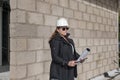 Architect wearing sunglasses and safety helmet at a construction site while holding the building plans and an electronic device Royalty Free Stock Photo