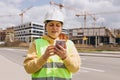 Young Architect woman in white hardhat and safety vest with digital tablet using smartphone outdoors. Female engineer Royalty Free Stock Photo