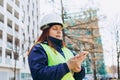 Architect woman in white hardhat and safety vest with digital tablet using smartphone outdoors. Female engineer Royalty Free Stock Photo