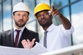 Architects in hardhats working with blueprint outside modern building Royalty Free Stock Photo