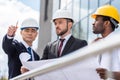 Architects in hardhats working with blueprint outside modern building