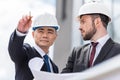 Architects in hardhats working with blueprint outside modern building Royalty Free Stock Photo