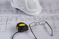 Architects workplace - architectural blueprints with measuring tape, safety helmet and glasses on table. Top view. Royalty Free Stock Photo