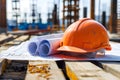 Architectural blueprints and orange safety helmet rest on a construction site