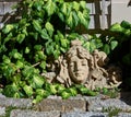 Architectural ornament of a woman`s face in a garden surrounded by ivy