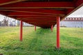 Architectural perspective from under a pedestrian bridge with red metal pillars on green grass. A conceptual view of a modern Royalty Free Stock Photo