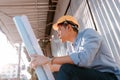 Architecture man sitting on the ground and hold blueprints design plan and wearing safety helmet at site construction in hot Royalty Free Stock Photo