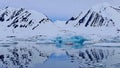 Arctic landscape with iceberg and reflections in the water of snowy mountains and blue sky, Svalbard archipelago, Norway