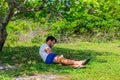 Young man reading in nature, sitting on the grass under a cashew tree Royalty Free Stock Photo