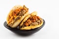 Arepas filled with shredded beef and pork rind served in a black ceramic dish