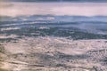 Arial view of snow covered terrain with mountains in the distance and a few low clouds over a river and a town and a highway somew Royalty Free Stock Photo