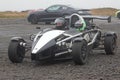 Ariel atom 2 seater open chassis space frame racing car with 2 passengers wearing helmets on a wet day