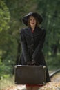 Aristocratic woman in black hat with suitcase in an autumn park. Middle-aged woman wears vintage clothes in retro style