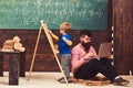 Arithmetic lesson at school. Kid writing on chalkboard while concentrated teacher works on laptop. Side view sitting man Royalty Free Stock Photo