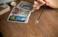 Arm of a dowser with hand-held pendulum on the background of a burning candle and tarot cards. Royalty Free Stock Photo