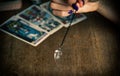 Arm of a dowser with hand-held pendulum on the background of tarot cards. Royalty Free Stock Photo