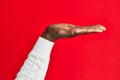 Arm and hand of african american black young man over red isolated background with flat palm presenting product, offer and giving