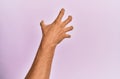 Arm and hand of caucasian young man over pink isolated background grasping aggressive and scary with fingers, violence and