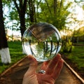 Arm holding the big transparent glass ball on the finger tips on the outdoor background Royalty Free Stock Photo