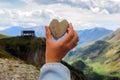 Arm holding the heart shaped stone in front of the wide view of high Caucasus Mountains beautiful landscape in Kazbegi, Georgia