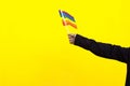 arm of an unrecognizable person waving holding a gay LGBT flag on a yellow background.