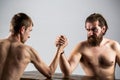 Arm wrestling. Heavily muscled bearded man arm wrestling a puny weak man. Arms wrestling thin hand, big strong arm in Royalty Free Stock Photo