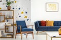 Armchair and couch with pillows in blue and orange living room interior with poster and plant. Real photo Royalty Free Stock Photo