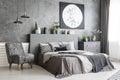 Armchair next to bed in grey bedroom interior with moon poster o