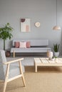 Armchair and wooden table in grey living room interior with post