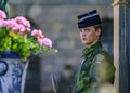 Armed forces female officer in camouflage uniform at Royal Palace guard post, flowers in foreground, Stockholm, Sweden