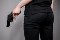 Armed girl in black jeans hides her pistols gun behind her back. Hidden threat Killer woman.