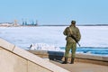 An armed Russian border guard guards the state border. View of a soldier from the back. Granite embankment of the Amur