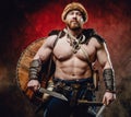 Muscular viking with naked torso and knives in dark red background