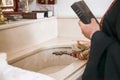 An Armenian priest with a cross and a bible performs the rite of baptism over the font