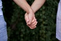 Arms of young couple in love, embracing. Close-up picture of romantic couple hands holding together in front of green leaves wall