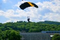An Army cadet paratrooper with a black and yellow parachute landing at West Point with trees and a school building in the Royalty Free Stock Photo