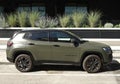 Army green Jeep Compass at the road side with some plants on behind.