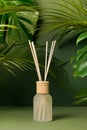 Aroma reed diffuser home fragrance with rattan sticks on green background with palm tropical leaves