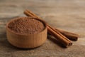 Aromatic cinnamon powder in bowl near sticks on wooden table, closeup Royalty Free Stock Photo
