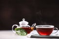 Aromatic hot tea in glass cup, teapot and leaves on white wooden table against black background. Space for text Royalty Free Stock Photo